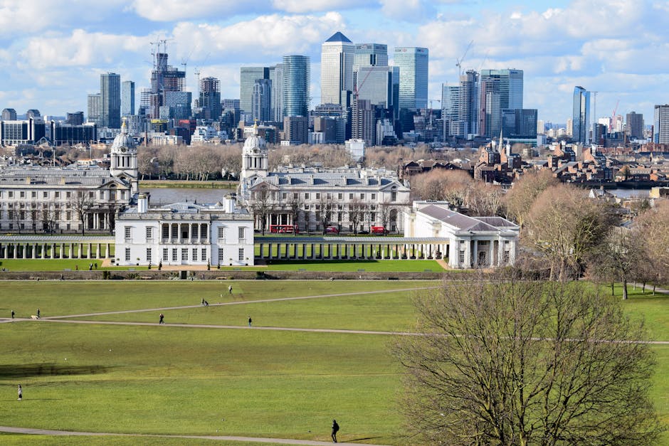 A wide view of a large historic white palace with classical architectural features, including columns, domed towers, and a colonnaded perimeter, situated on a well-maintained green lawn with walking p